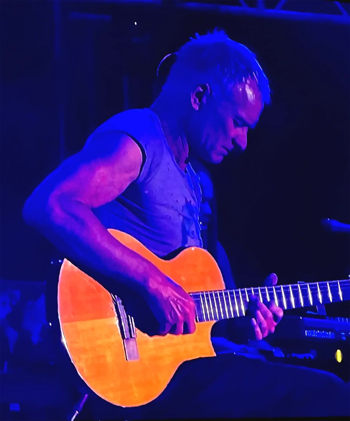 Sting playing an acoustic guitar under blue stage lights